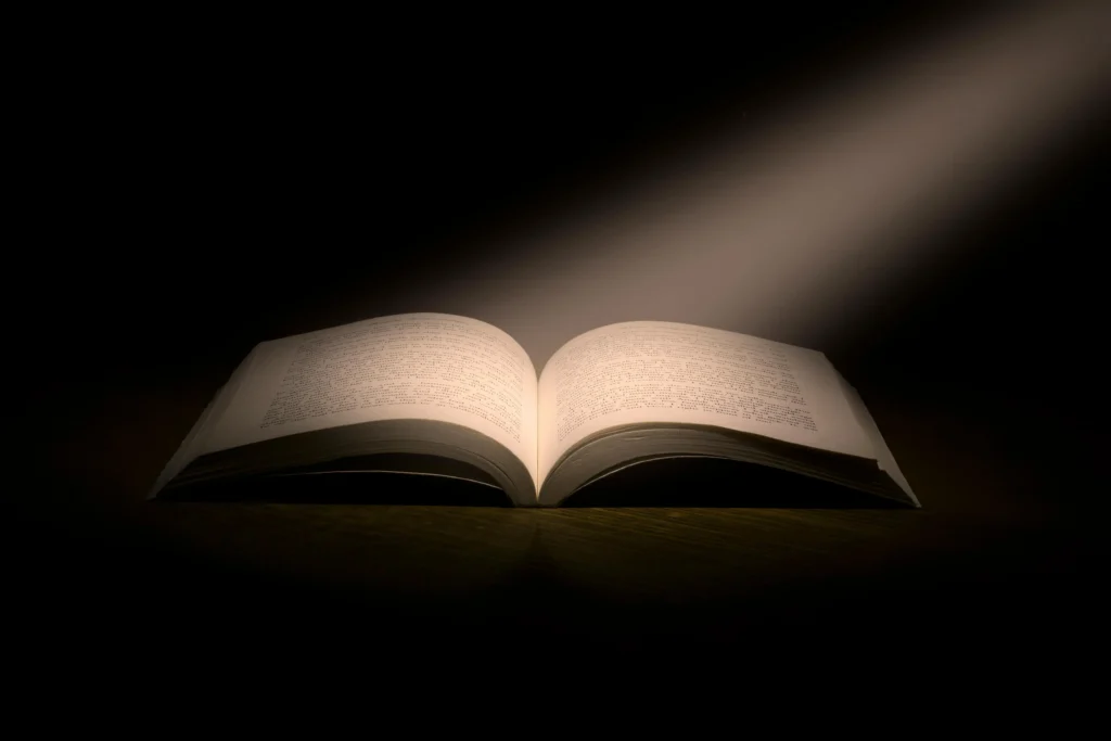 An open Bible on a wooden table with sunlight streaming in through a window